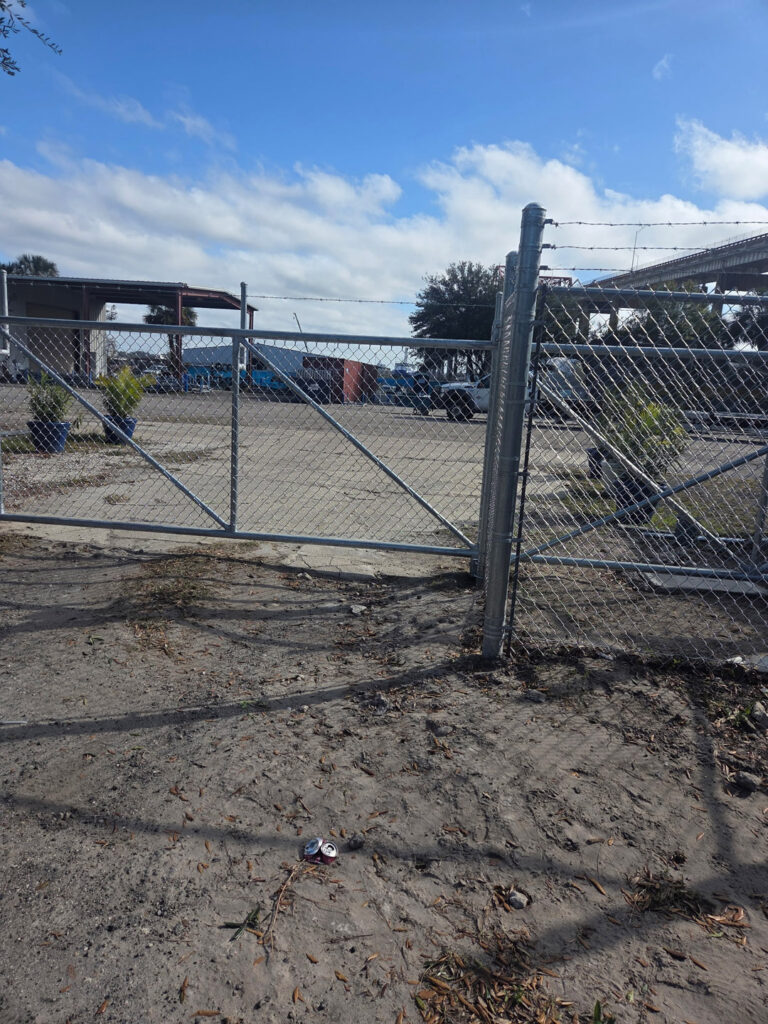 Metal chain-link gate with barbed wire, outdoor fencing in sunlight.