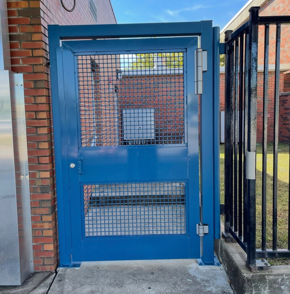 Durable blue metal gate with mesh panels at entrance to fenced outdoor area.