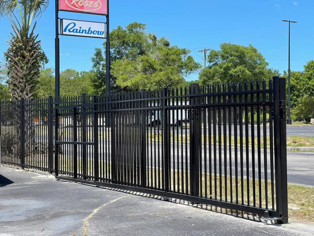Black metal security fence with a gate in front of a parking lot.
