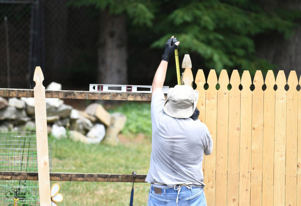 Installing a wooden privacy fence with tools and measuring tape in yard.