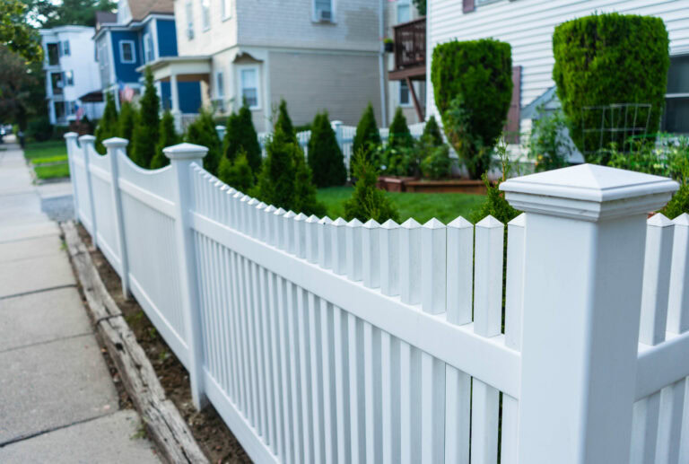 White picket fence along a sidewalk in a residential neighborhood.