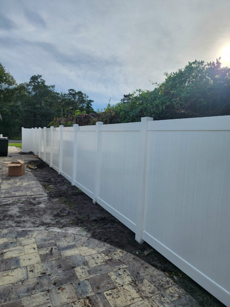 Solid white privacy vinyl fence with decorative caps, installed on a paved backyard.